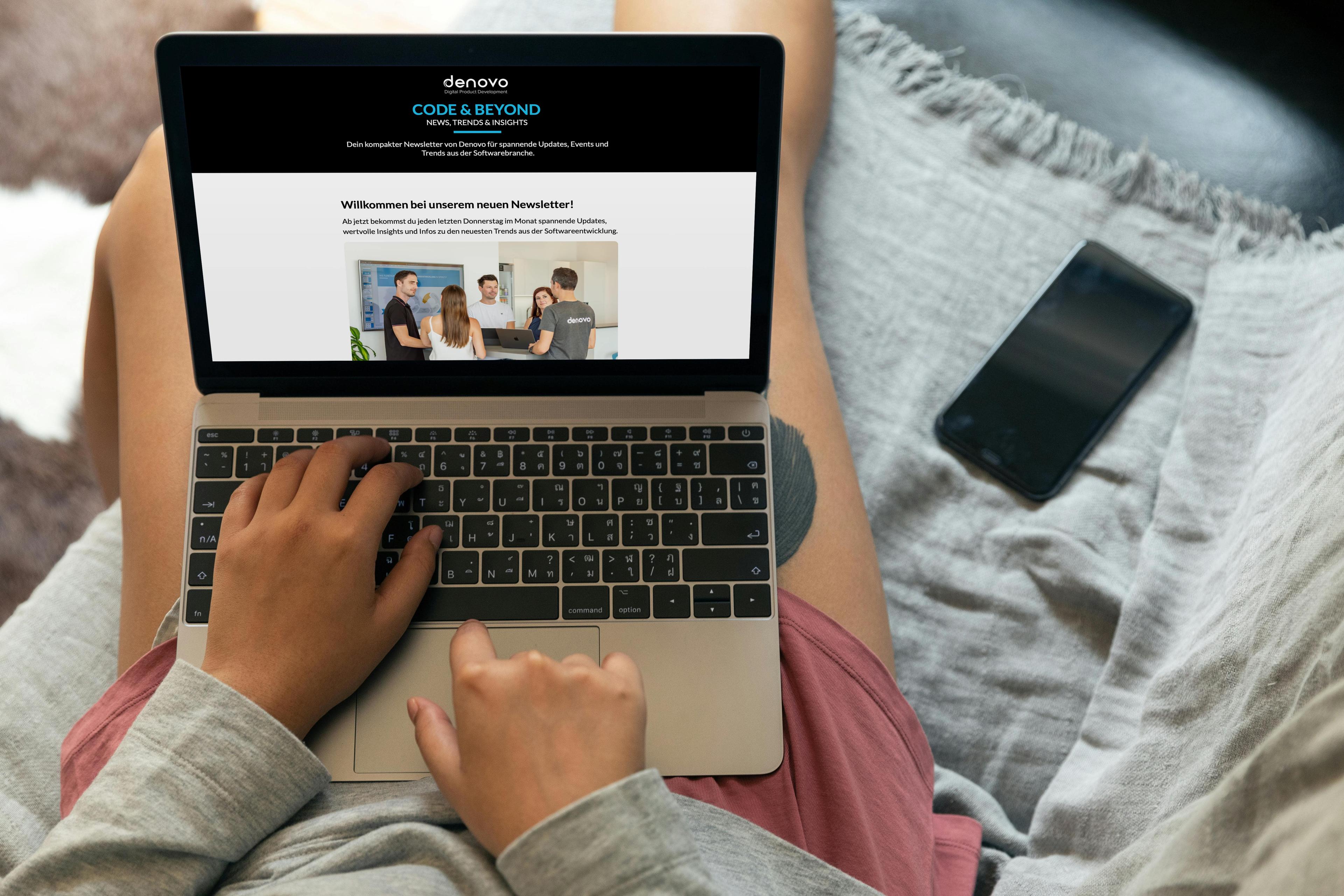A man sits with a laptop on his lap and looks at a preview of the Denovo newsletter.